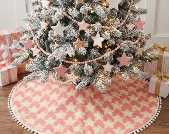 Könnte beinhalten: Ein geschmückter Weihnachtsbaum mit sternförmigen Ornamenten und einem rosa-weiß gemusterten Baumrock. Der Baum ist mit rosa und weißen Sternornamenten, einer rosa Perlenkette und Lichtern geschmückt. Geschenkboxen sind sichtbar.