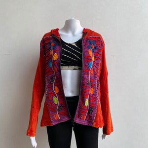 Pode incluir: Um moletom vermelho com zíper com um design de bordado floral roxo, laranja e verde. O moletom tem capuz e mangas compridas.