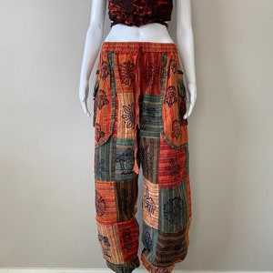 May include: Patchwork printed pants with a drawstring waist and side pockets. The pants are in shades of orange, red, green, and brown with a floral and mushroom design.