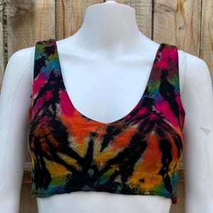 May include: A tie-dye crop top with a scoop neck and thin straps. The top is a mix of black, orange, yellow, pink, and blue.