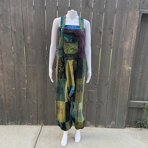 Könnte beinhalten: Grün, blau und braune Patchwork-Latzhosen mit Blumenmuster. Die Latzhosen haben eine große Tasche vorne und verstellbare Träger.