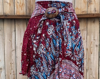 Puede incluir: Una falda color granate con estampado paisley azul y blanco. La falda tiene una cinturilla ancha con una hebilla de madera.