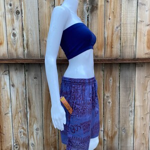 May include: Purple and red patterned shorts with a drawstring waist. The shorts have a pocket on the side with a small orange and yellow package sticking out. The shorts are on a white mannequin against a wooden background.
