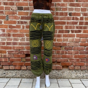 May include: Green trousers with black stripes and yellow embroidery. The trousers have a drawstring waist and a loose fit.