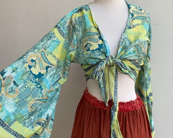 May include: A green and yellow paisley print top with a tie front and long bell sleeves. The top is cropped and is being worn with a brown tiered skirt.