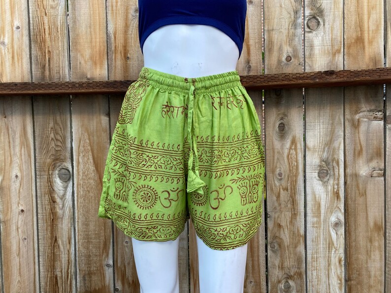 May include: Green cotton shorts with a brown print of Sanskrit symbols and designs. The shorts have a drawstring waist and a relaxed fit.