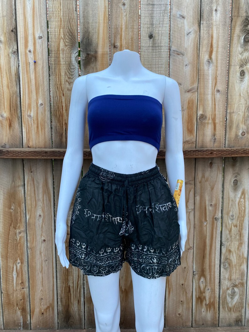 May include: Black and white printed shorts with a stretchy waistband. The shorts have a pattern of Sanskrit writing and other symbols. The shorts are being modeled on a white mannequin.