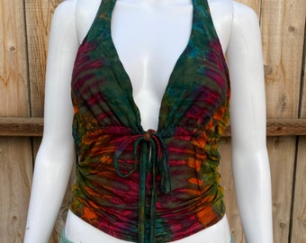 Puede incluir: Un top de halter con un lazo en la parte delantera. El top está hecho de una tela elástica con un patrón de tie-dye en tonos de verde, naranja, rojo y morado.