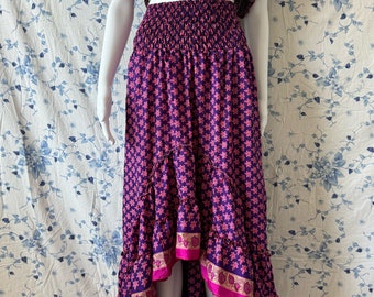Puede incluir: Una falda maxi de estampado morado y rosa con un dobladillo alto-bajo. La falda tiene una cintura elástica fruncida y un ribete rosa y dorado.