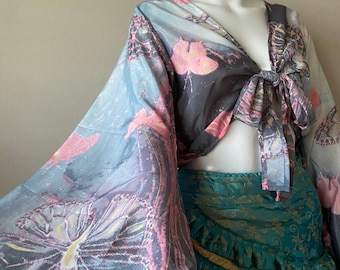 Puede incluir: Un top corto con lazada delantera con estampado de mariposa en tonos azules, rosas y grises. El top tiene mangas largas y anchas y un corte holgado.