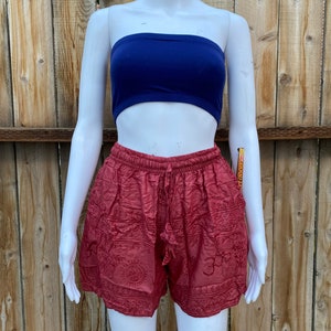 May include: Red cotton shorts with embroidered floral and geometric patterns. The shorts have a drawstring waist and a relaxed fit.