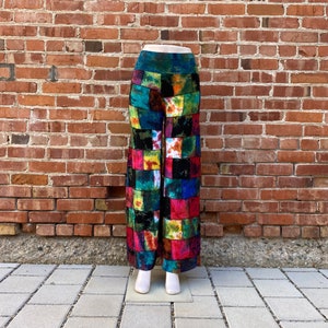 May include: Colorful patchwork pants with a wide leg design. The pants feature a vibrant mix of squares in various colors, including red, blue, green, and yellow. The fabric appears to have a tie-dye effect in some of the squares. The pants are displayed on a mannequin.