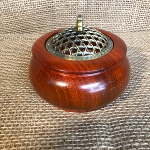 May include: A round wooden incense burner with a brass lid and a decorative design. The lid has a mesh top and a small handle.
