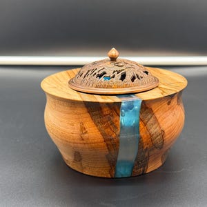 May include: A wooden incense burner with a blue resin inlay and a decorative metal lid. The lid has a floral design.