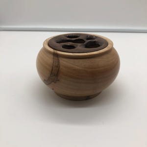 May include: A small wooden bowl with a brown wood top. The top has five holes cut out of it.