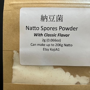 Op de afbeelding: Close-up van een bruin zakje met een wit etiket. Het etiket luidt "Natto Spores Powder With Classic Flavor" en bevat Japanse karakters. Het zakje bevat 2g poeder, goed voor maximaal 20kg Natto.