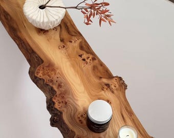 May include: A wooden tray with a natural wood grain finish sits on a white bathtub. The tray has a white ceramic vase with a dried branch of red leaves. There is a small white jar and a white candle on the tray.