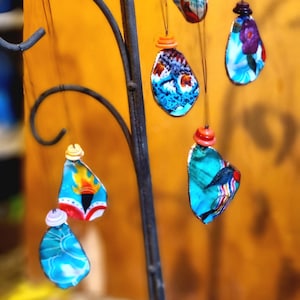 May include: Six colourful, patterned ornaments hang from a black metal stand. Each ornament is a unique shape and features a different design. The ornaments are made of fabric and have a vintage aesthetic.