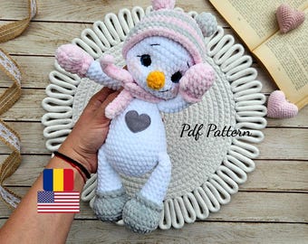 Puede incluir: Un muñeco de nieve blanco hecho a mano con un corazón gris, que lleva un gorro, una bufanda y manoplas rosas y grises. El muñeco de nieve tiene una nariz de zanahoria amarilla y ojos negros. El texto "Pdf Pattern" es visible.