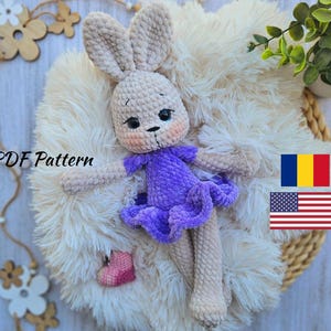 May include: Crocheted bunny amigurumi toy wearing a purple dress. The bunny is sitting on a white fluffy surface. The image includes the text "PDF Pattern".