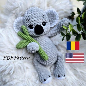 May include: A handmade gray crochet koala bear holding a green crochet branch. The koala has a black nose and eyes, and white accents on its ears and feet. The text "PDF Pattern" is visible.