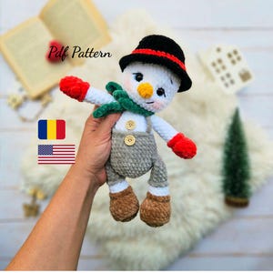 Könnte beinhalten: Gehäkelte Schneemann-Puppe mit schwarzem Hut, roten Fäustlingen und grünem Schal. Der Schneemann hat eine Karottennase und Knopfaugen. Die Puppe trägt eine graue Latzhose und braune Stiefel. Der Text "Pdf Pattern" ist im Bild sichtbar.