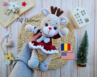 May include: A crocheted reindeer doll with a red dress, white trim, and a heart-shaped detail. The doll has brown antlers, a red nose, and gray shoes with red star accents. The text "Pdf Pattern" is visible.