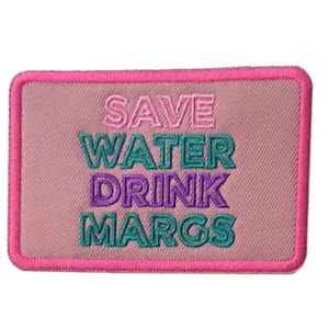 May include: A rectangular patch with a pink background and a bright pink border. The text "SAVE WATER DRINK MARGS" is embroidered in pink, teal, and purple thread. The patch is likely for a jacket or bag.