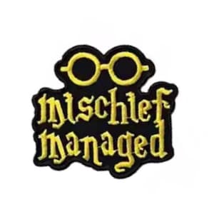 May include: A black patch with the words "mischief managed" in yellow, stylized lettering. Above the text are yellow-rimmed glasses. The patch has a black border and is likely an accessory for clothing or bags.