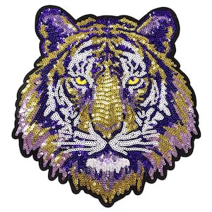 May include: A sequined tiger head patch with a black border. The tiger's face features purple, gold, and white sequins, with yellow eyes. The design is detailed and suitable for embellishing clothing or accessories.
