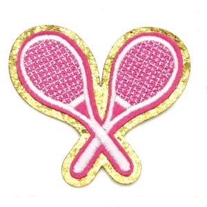 May include: Embroidered patch featuring two crossed tennis rackets. The rackets are pink with white detailing, set against a gold glitter background. Ideal for decorating clothing or accessories, this patch adds a sporty touch.
