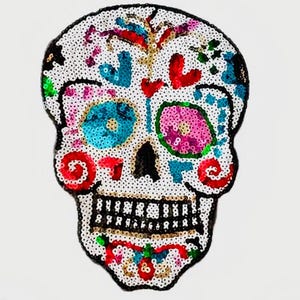 May include: A Day of the Dead sugar skull patch, embellished with colorful sequins. The skull features turquoise, pink, red, and green accents, with a black outline and a white background. The design includes hearts, swirls, and floral elements.