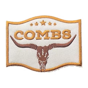 May include: Embroidered patch with a white background and a gold border. The patch features the word "COMBS" in gold block letters above a brown steer skull with long horns. Three gold stars are above the word "COMBS".
