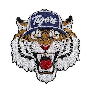 May include: A sequined tiger patch with a navy blue baseball cap that reads "Tigers" in white script. The tiger has a gold, black, white, and red color scheme, with an open mouth and visible teeth.