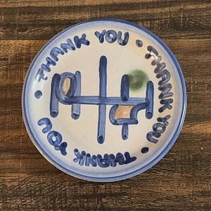 Puede incluir: Un plato de cerámica blanco con borde azul y diseño abstracto azul y naranja en el centro. Las palabras "THANK YOU" están escritas en azul alrededor del borde del plato.
