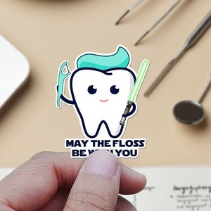 May include: A white cartoon tooth character holding a green lightsaber and a dental floss pick. The text reads "May the floss be with you".