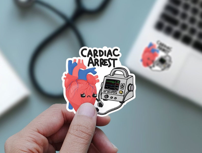 May include: A sticker featuring a cartoon heart and a defibrillator. The heart is red with a blue vein and has a sad face. The defibrillator is grey with a black screen and a black cord. The sticker reads "Cardiac Arrest" in black text.