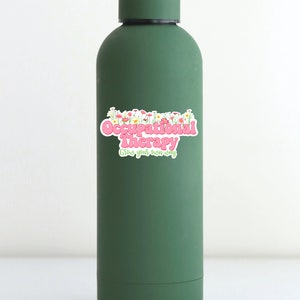 Pode incluir: Garrafa de &aacute;gua reutiliz&aacute;vel verde com um adesivo rosa e branco que diz "Occupational Therapy Grow your own way" com um design floral.