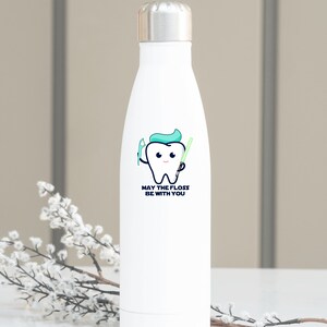May include: White stainless steel water bottle featuring a cartoon tooth holding a toothbrush and a lightsaber. The text on the bottle reads "May the floss be with you."
