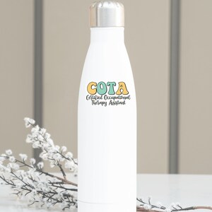 Pu&ograve; includere: Bottiglia d'acqua in acciaio inox bianca con una grafica colorata che dice "COTA Certified Occupational Therapy Assistant".