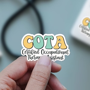 Pu&ograve; includere: Un adesivo con il testo "COTA Certified Occupational Therapist Assistant" in un font colorato e scritto a mano. Le lettere COTA sono in grandi lettere maiuscole a forma di bolla con un contorno giallo e un riempimento blu chiaro. Il resto del testo &egrave; in nero.