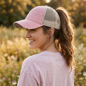 May include: A dusty pink baseball cap featuring a beige mesh back panel and a curved brim with a small floral pattern on the underside. The cap has a structured front panel and a classic six-panel design with a button on the top center.