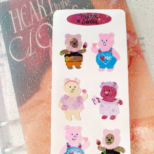 May include: A sheet of stickers featuring cute cartoon bears with different expressions and outfits. The stickers are designed with a pastel color scheme and feature the text "me x Stella".