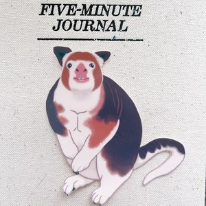 May include: A cartoon illustration of a red, white, and black animal with a long tail. The animal is sitting on a white background with the text "The Five-Minute Journal" above it.