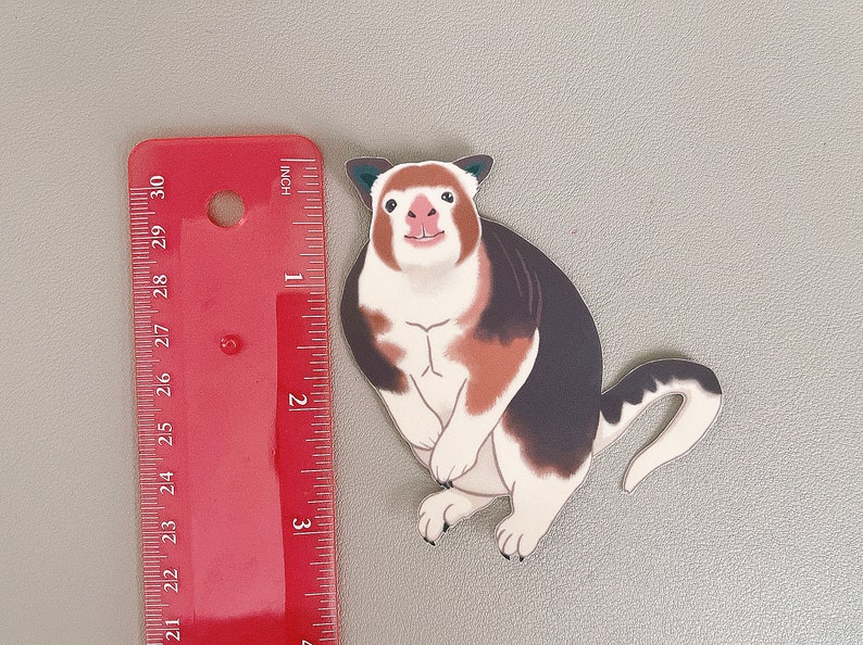 May include: A white, brown, and black cartoon animal with a long tail. The animal has a white face with a pink nose and a wide smile. The animal is about 3 inches tall.