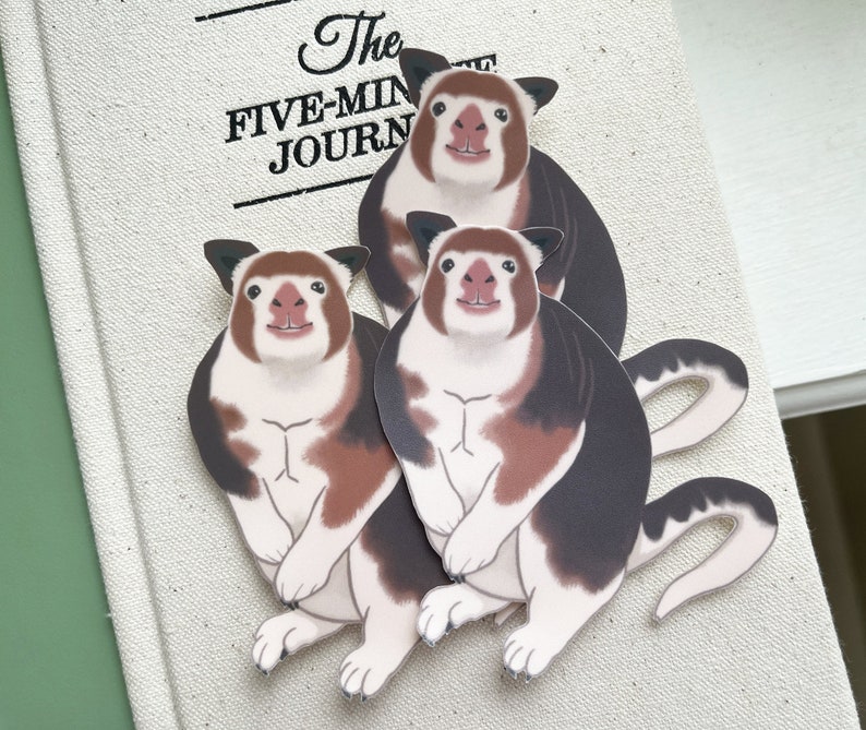 May include: Three cartoon stickers of a white and brown animal with black markings. The animal has a long tail and a round body. The stickers are on a white background with the text "The Five-Min Journ" visible.