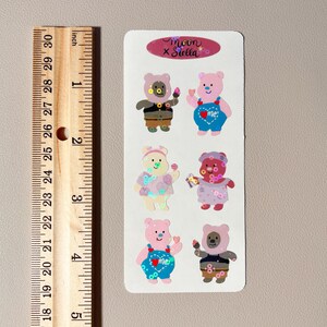 May include: A sheet of stickers featuring six adorable cartoon bears wearing different outfits. The bears are pink, brown, and white with colorful details. The stickers are labeled "moon x stella".
