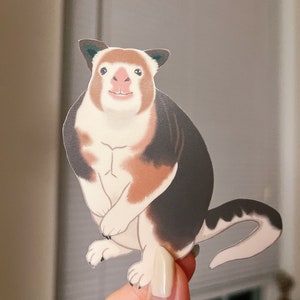 May include: A sticker of a cartoon kangaroo with brown, white, and black fur. The kangaroo is standing on its hind legs with its front paws tucked in. It has a pink nose and a friendly expression.