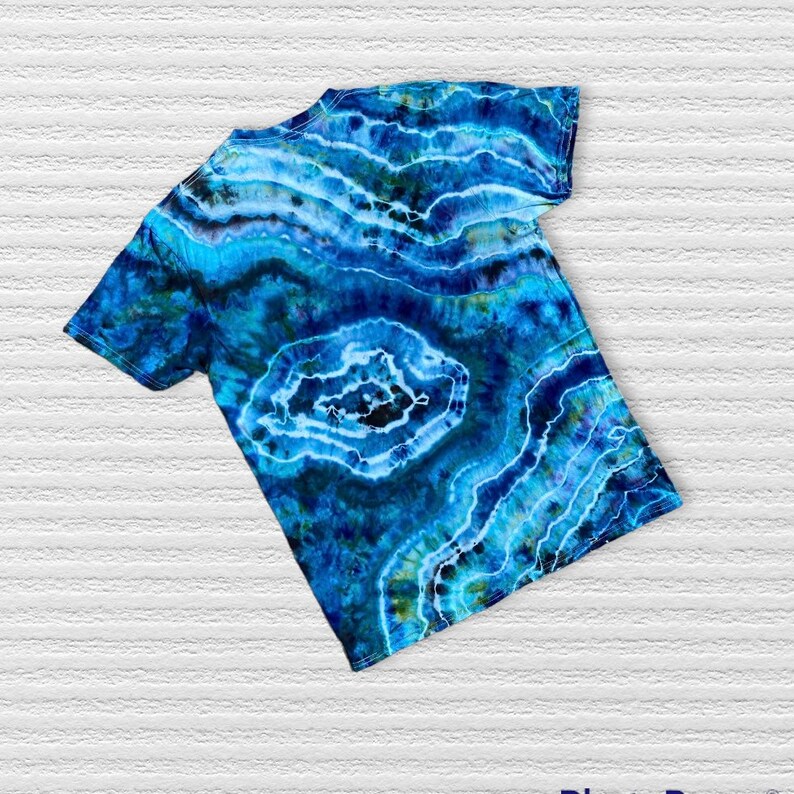 May include: A blue tie-dye t-shirt with a swirling pattern reminiscent of agate stone. The shirt has short sleeves and a crew neck.