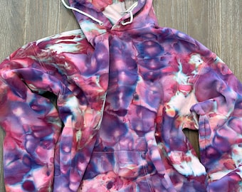 May include: A tie-dye hoodie in shades of purple, pink, and white. The hoodie has a drawstring hood and a kangaroo pocket.